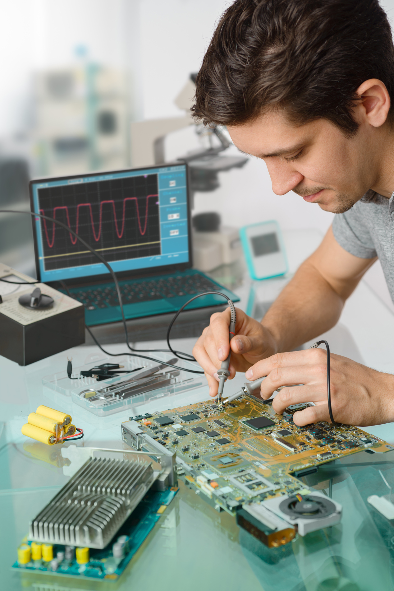 Young energetic male tech or engineer repairs electronic equipment in research facility. Shallow DOF, focus on the face of the worker.